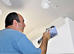 a handyman muds a newly installed piece of ceiling drywall